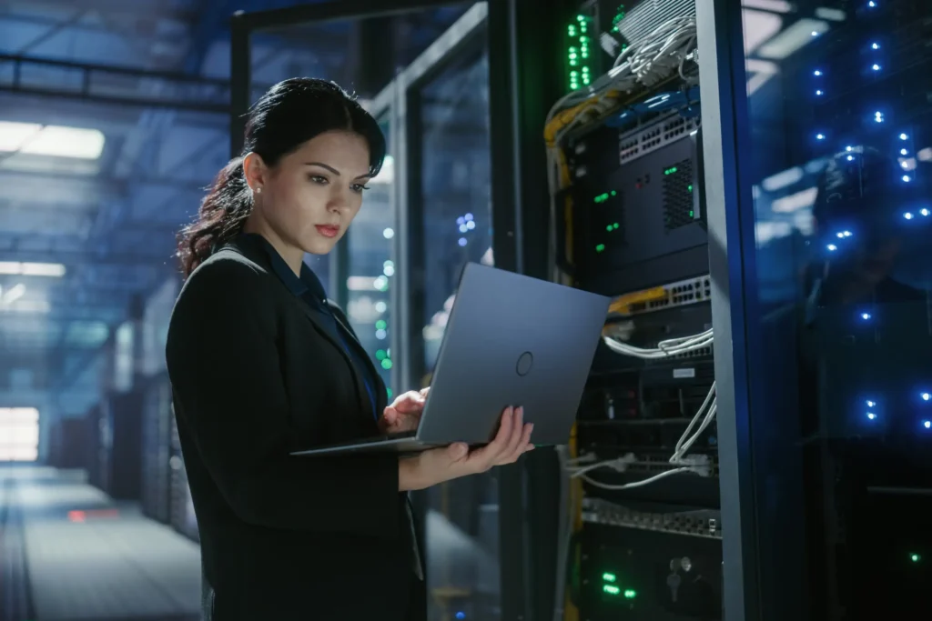 Professional working on laptop in modern server room with illuminated racks and network equipment — CXbuildr office infrastructure design and construction services.